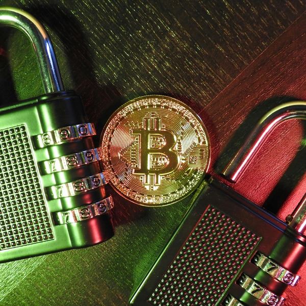 Bitcoin coin resting on a padlock and hardware parts
