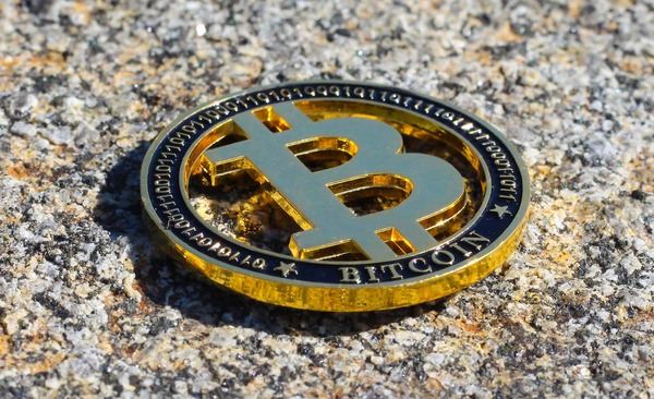 Gold Bitcoin coin lying on a speckled stone surface