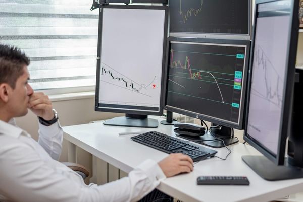 Trader at a desk with multiple monitors showing charts