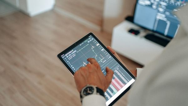 Hand using a tablet with a trading chart on screen