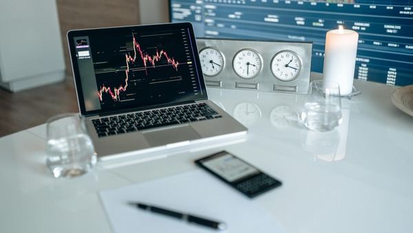 Laptop with a price chart on a white desk next to clocks