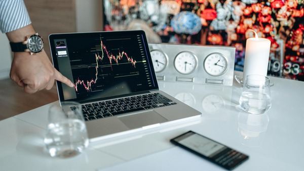 Hand pointing at a laptop chart next to desk clocks