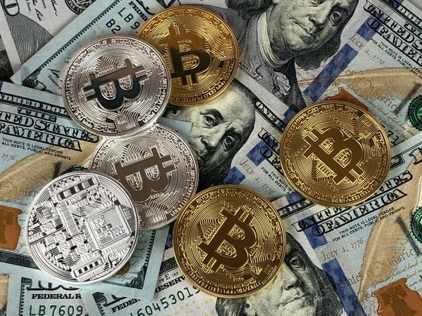Silver and gold Bitcoin coins scattered over US dollar bills