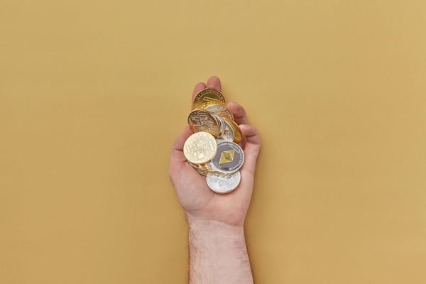 Hand holding a handful of crypto coins on a yellow background