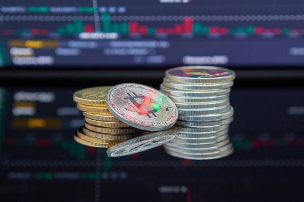 Stacks of crypto coins in front of trading charts