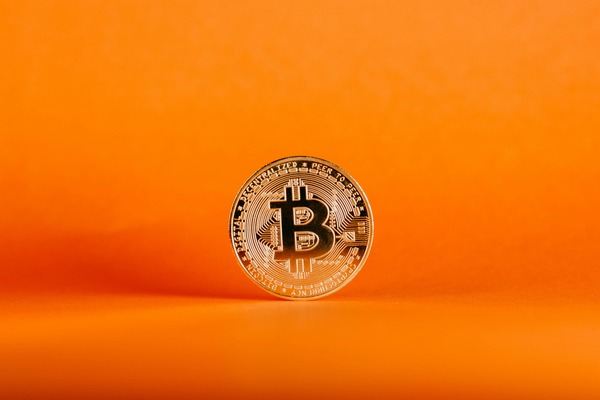 Single Bitcoin coin standing on a bright orange background